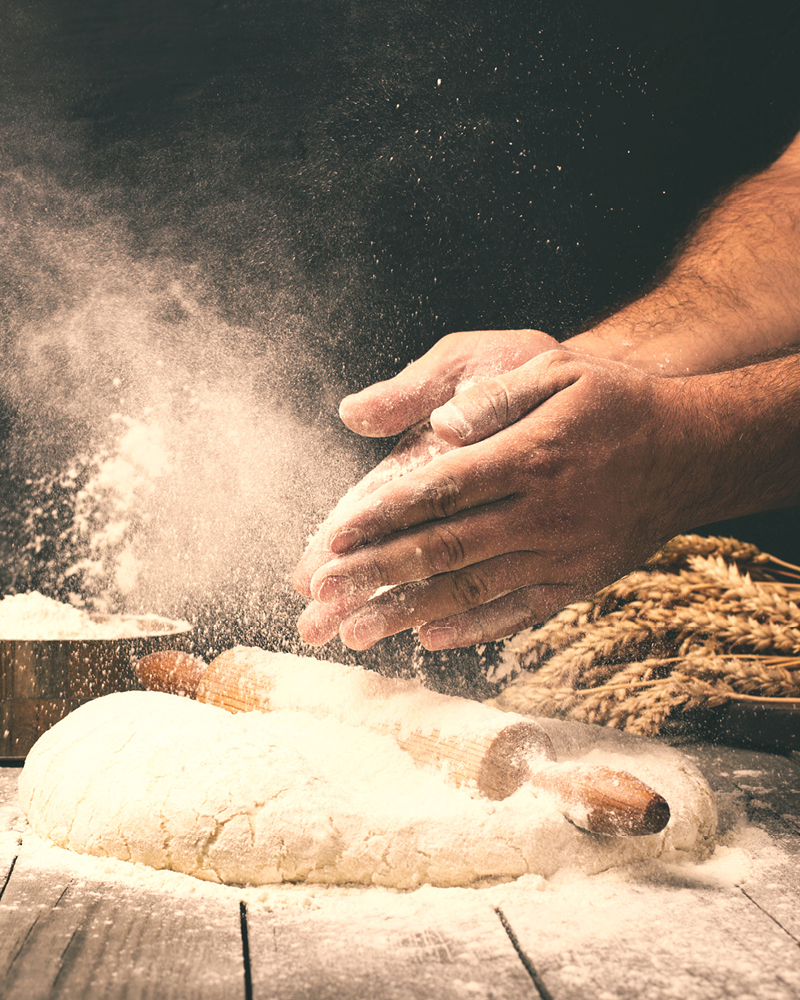 Bild der Produktion von Brot es sind zwei Hände zu sehen die Mehl über einem Brot verteilen